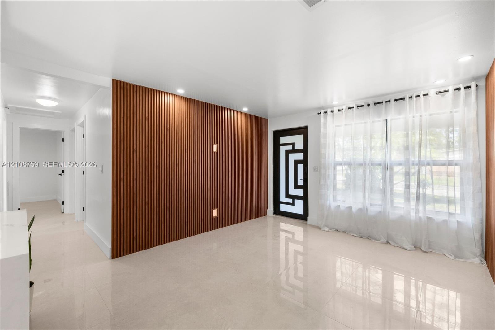 Interior space featuring a slatted wood-paneled accent wall, polished tile flooring, recessed ceiling lighting, and a front entry door with geometric glass inserts