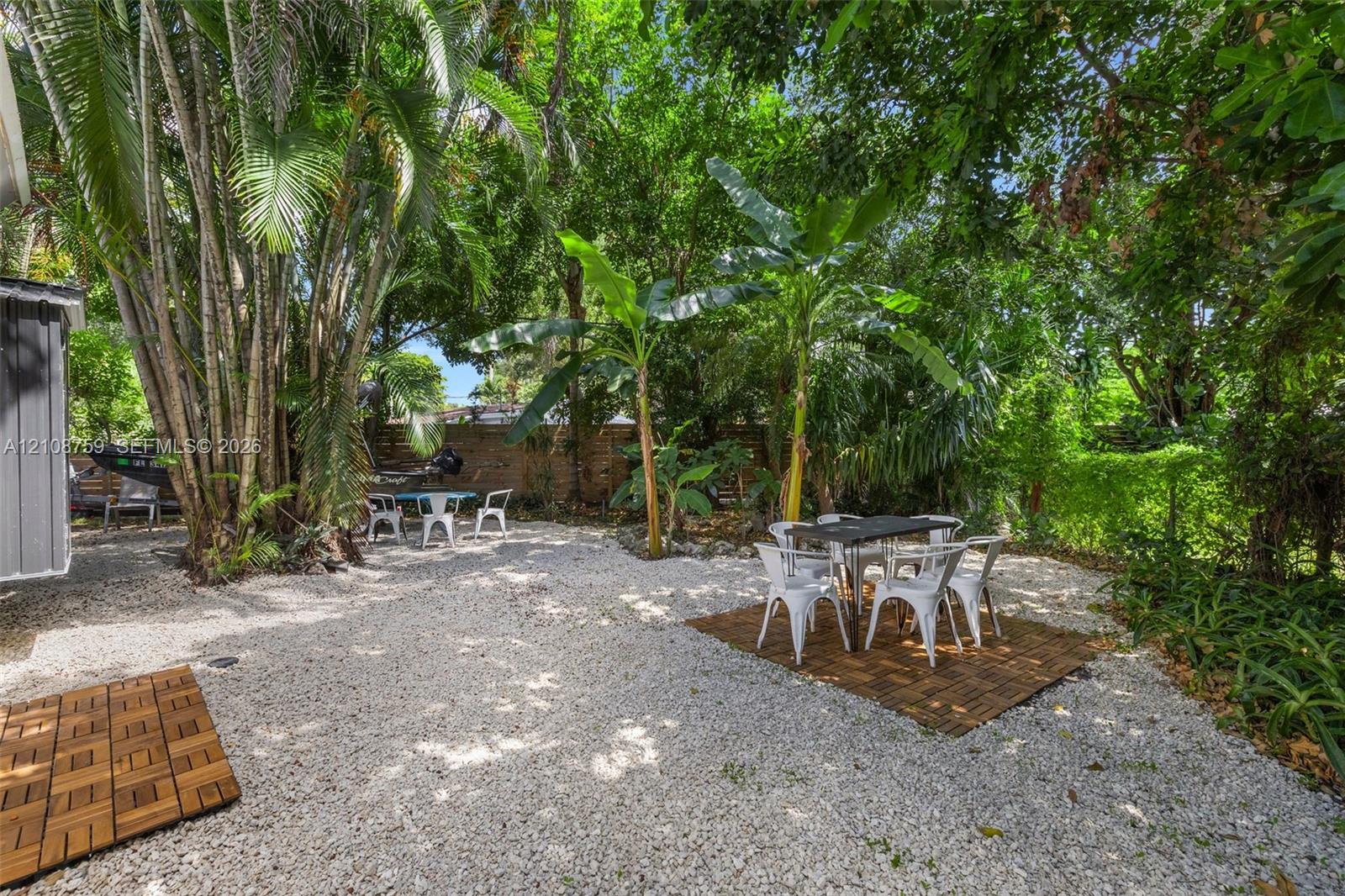 Private backyard featuring a crushed stone surface, interlocking wood-finish deck tiles, a perimeter masonry wall, and established tropical landscaping