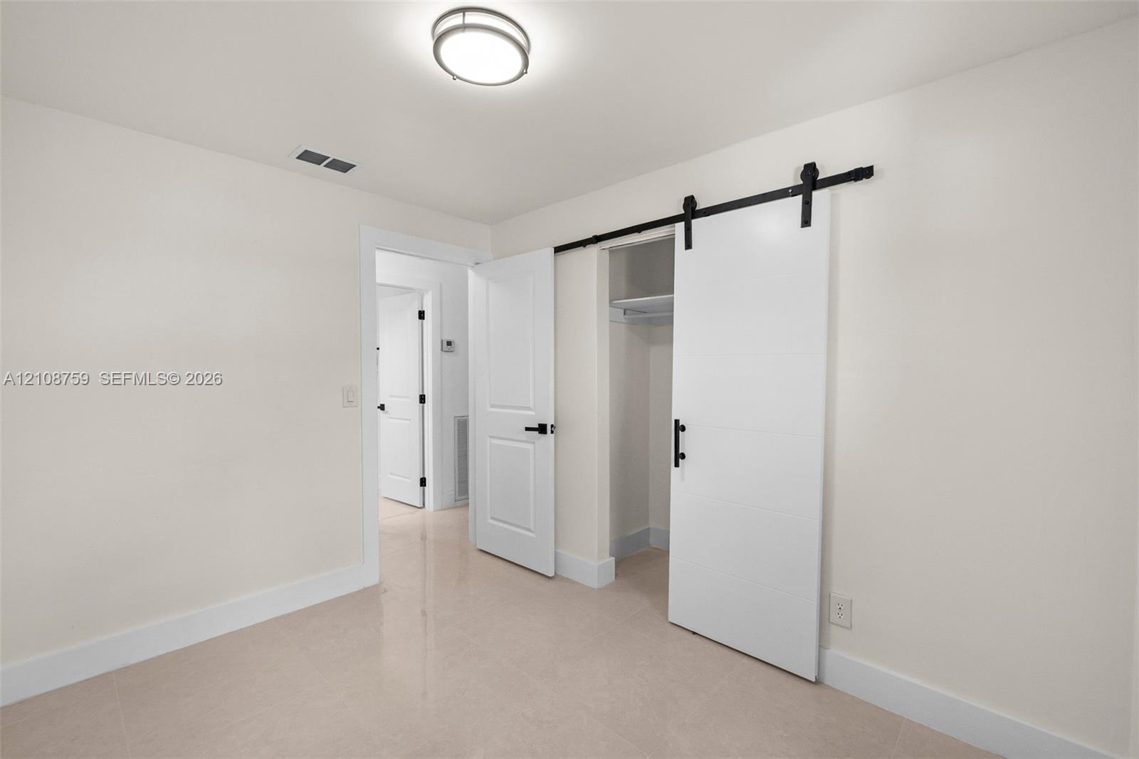 Room featuring a sliding barn-style door, matte black hardware, flush-mount ceiling light fixture, and solid-core interior doors