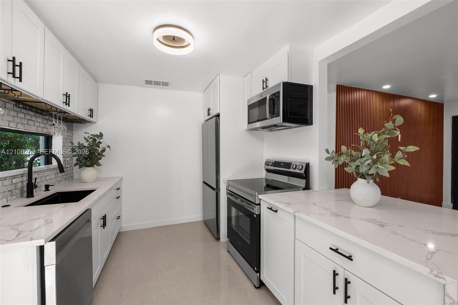 Kitchen featuring white shaker-style cabinetry, quartz countertops with veining, subway tile backsplash, stainless steel appliances, and matte black hardware