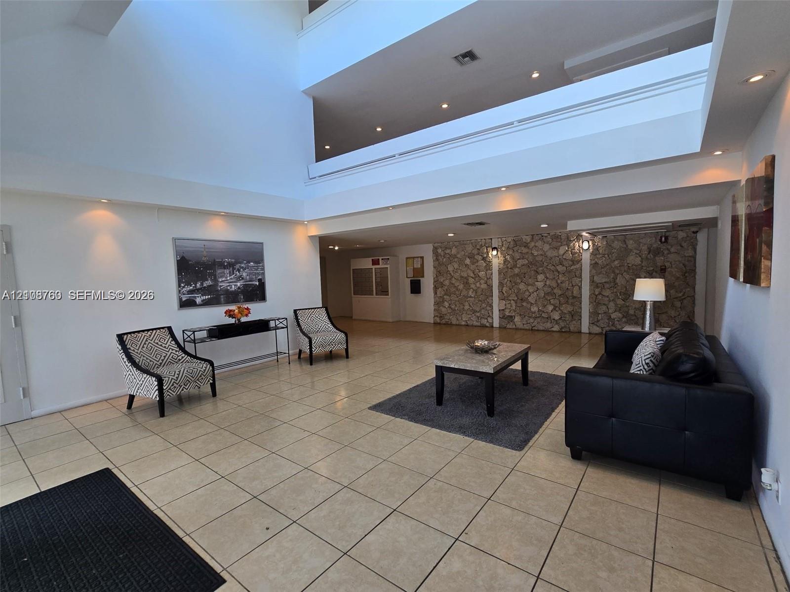 Expansive two-story foyer featuring soaring ceilings, tile flooring, a prominent natural stone accent wall, and recessed lighting
