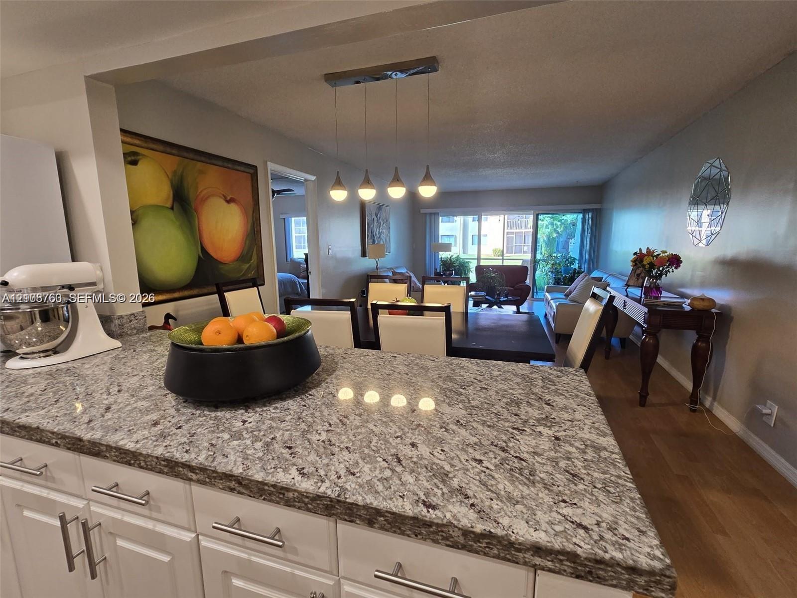Kitchen featuring a stone-finish countertop, white cabinetry with metallic hardware, and a four-light pendant fixture