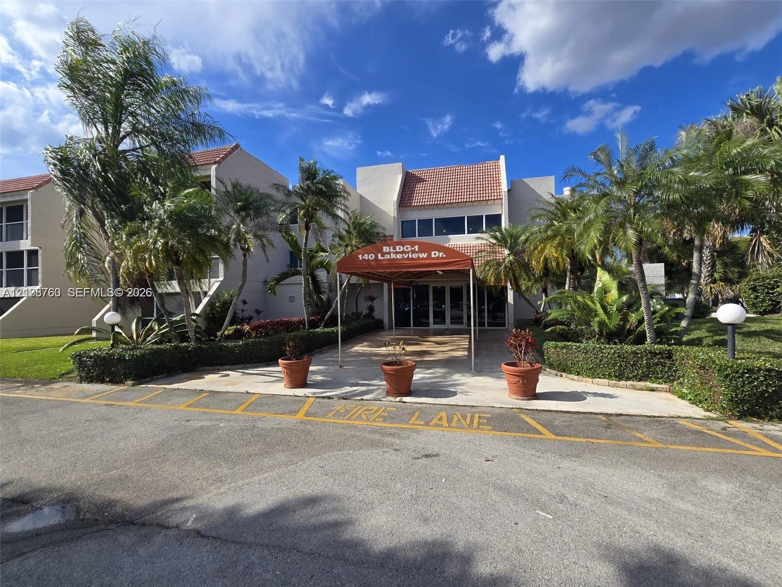 Multi-story exterior featuring a tile roof, covered building entrance, and mature tropical landscaping