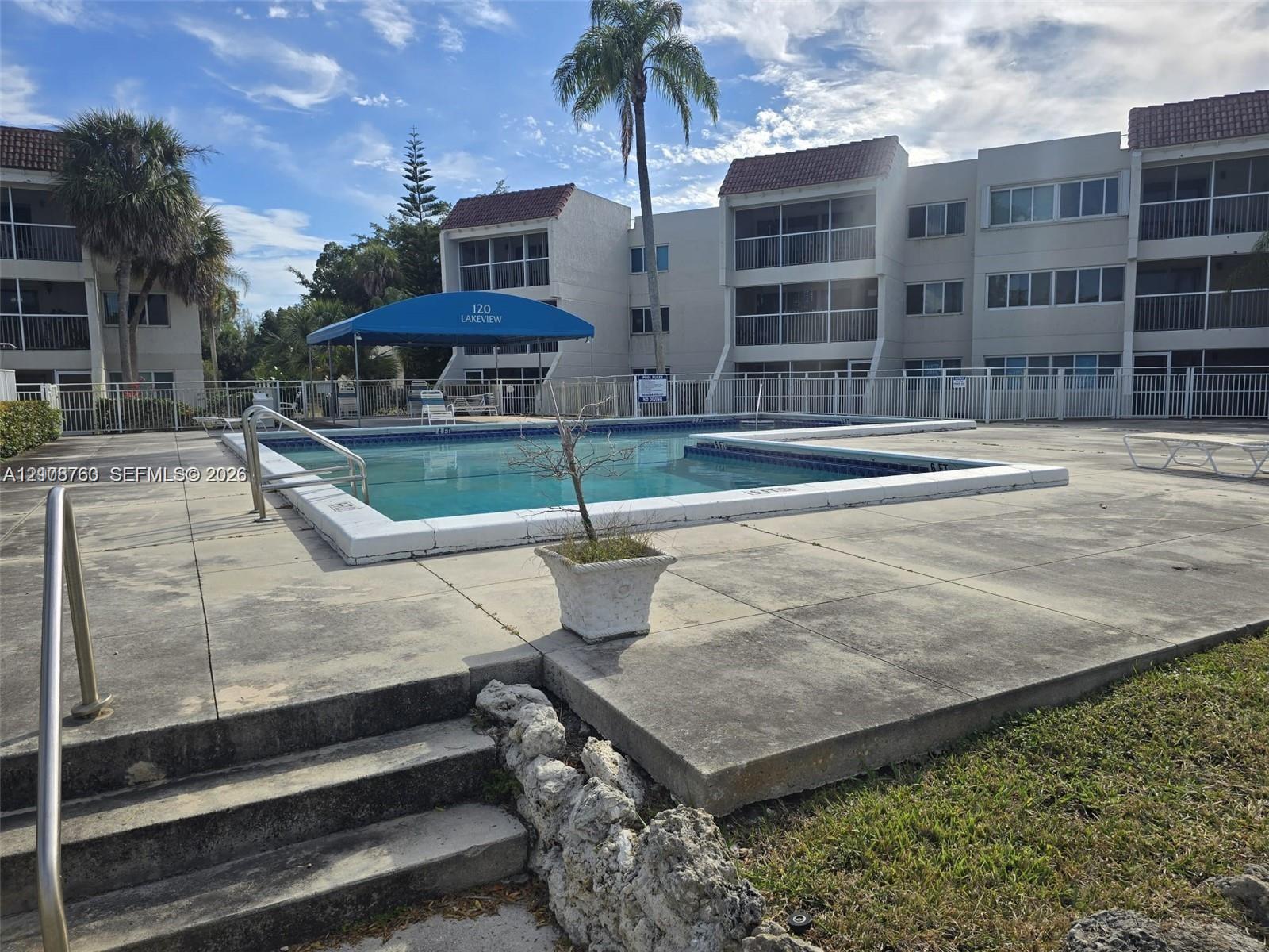 In-ground swimming pool featuring a concrete deck, metal safety fencing, and tiered stone-accented hardscaping