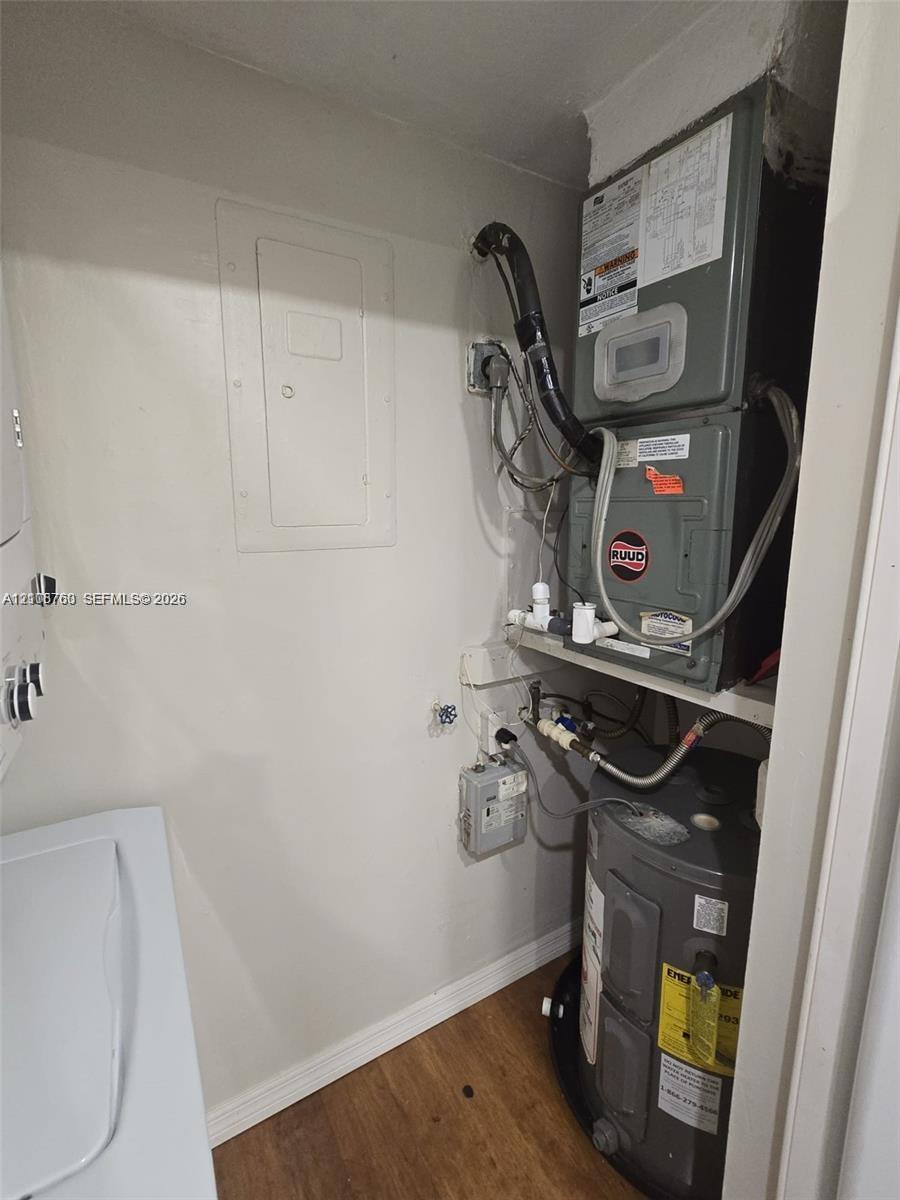Utility closet featuring a stacked air handling unit, water heater, electrical service panel, and wood-finish flooring