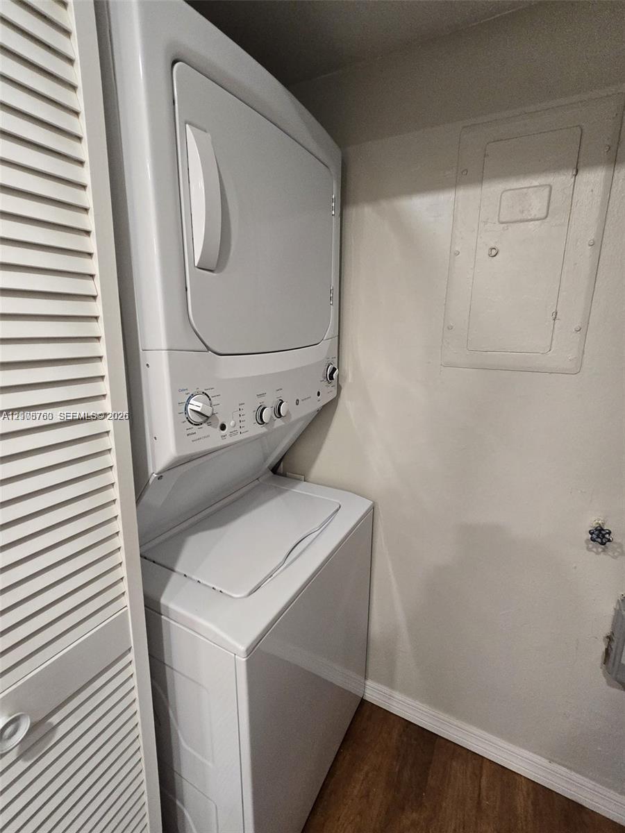 Stacked laundry appliance with white finish, housed within a closet featuring louvered doors and wood-finish flooring