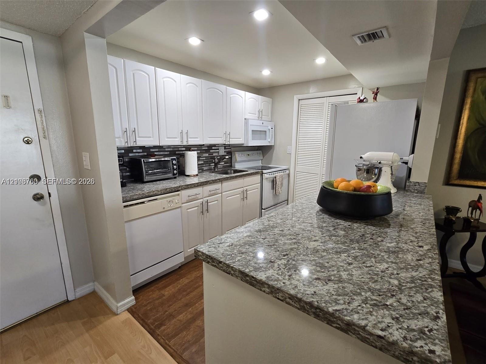 Kitchen featuring white cabinetry, stone-finish countertops, tile backsplash, recessed lighting, and wood-finish flooring