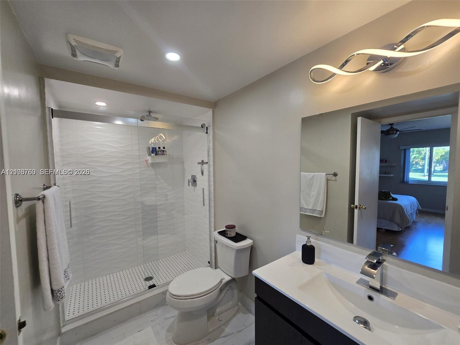 Bathroom featuring a vanity with an integrated basin, a walk-in shower with textured tile surround, glass sliding doors, and modern light fixtures