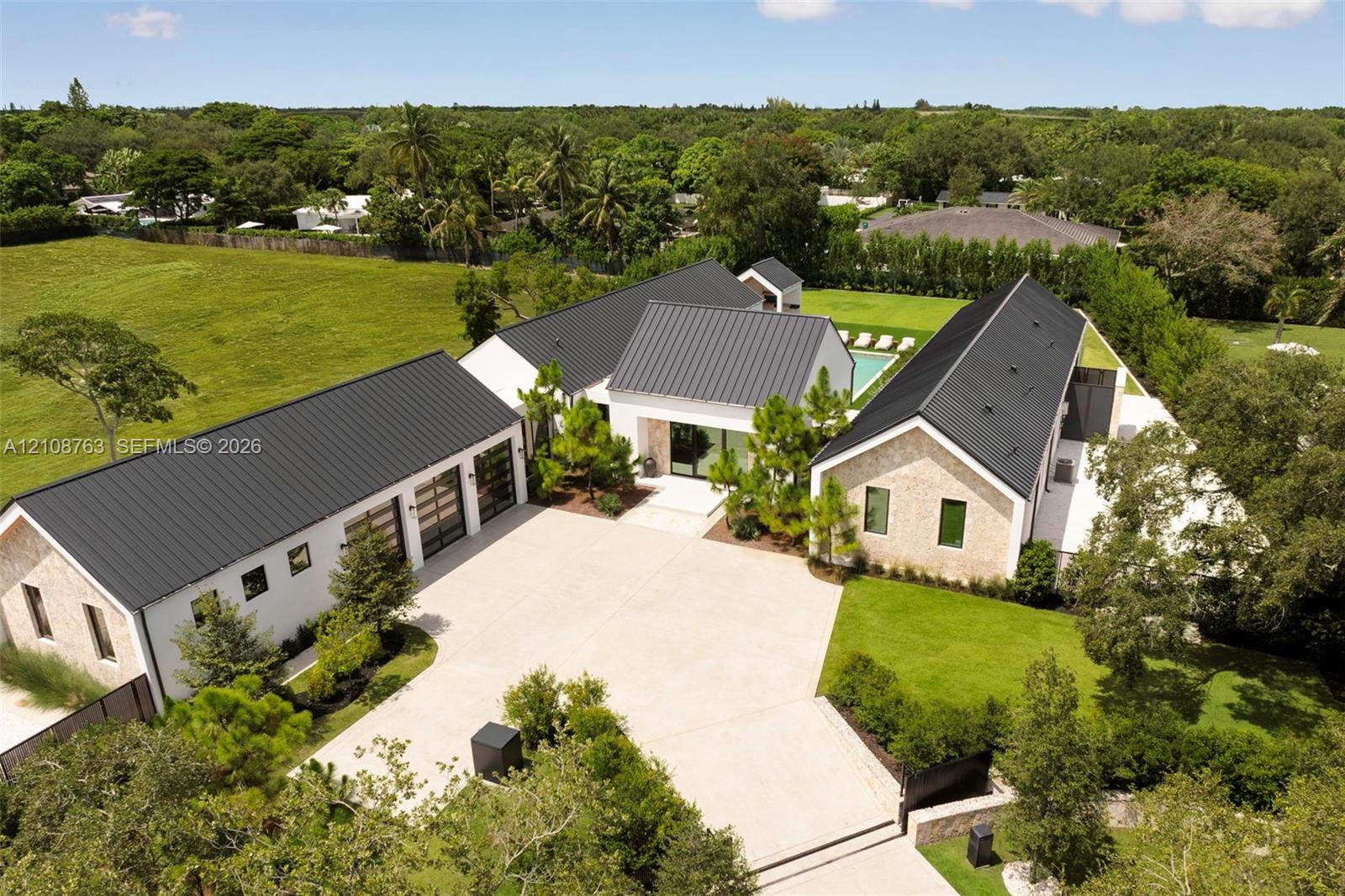 Modern estate featuring a metal roof, stone exterior, three-car garage with glass panel doors, private swimming pool, and extensive grounds