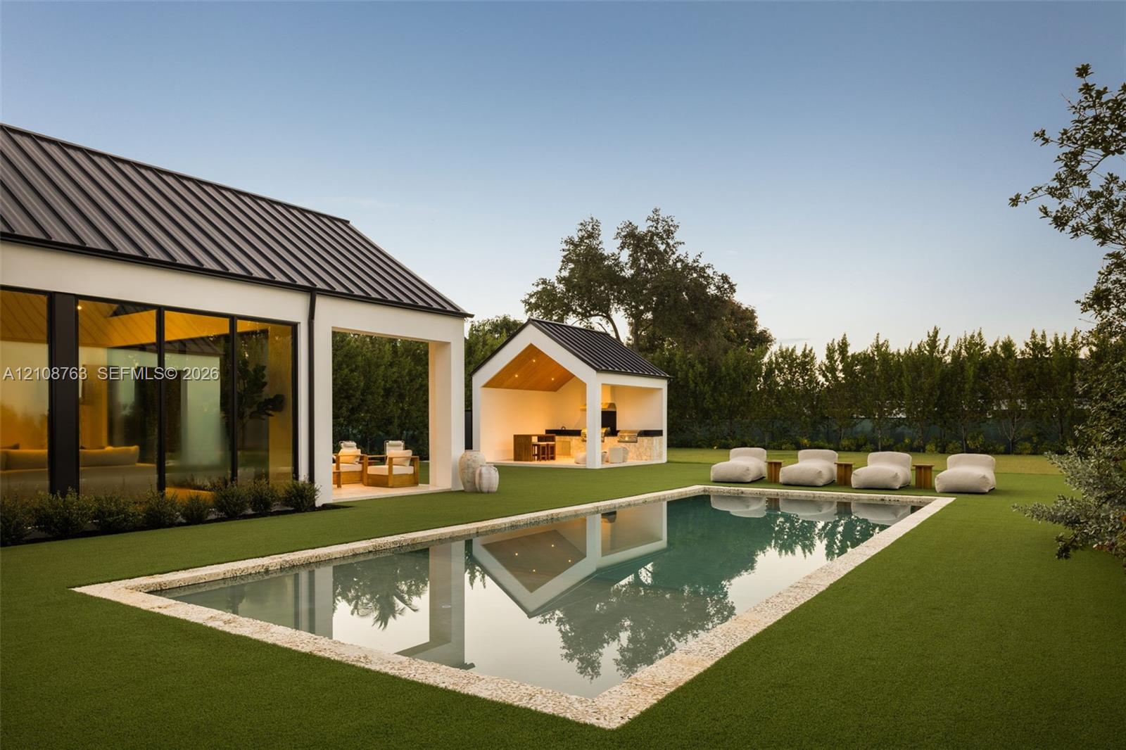 Outdoor space featuring a rectangular swimming pool with a stone coping, a detached open-air pavilion with built-in kitchen cabinetry, floor-to-ceiling glass wall panels, and a metal roof