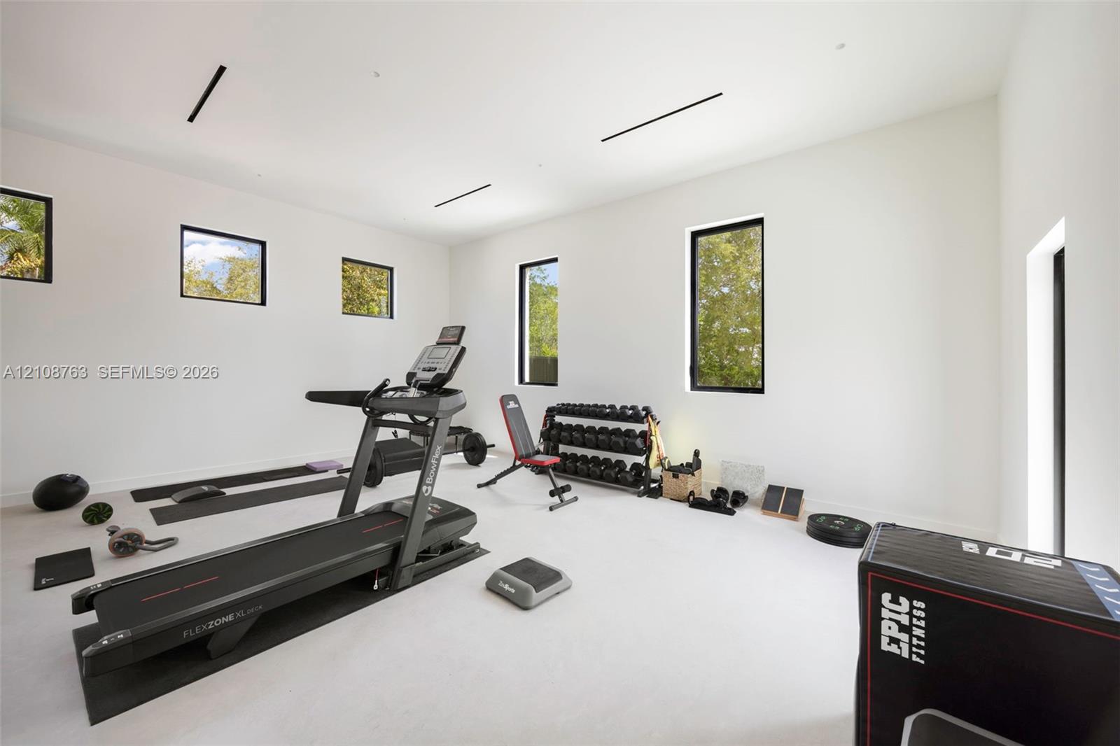 Spacious interior room with high ceilings, neutral wall finishes, recessed linear lighting, and multiple window installations with black frames