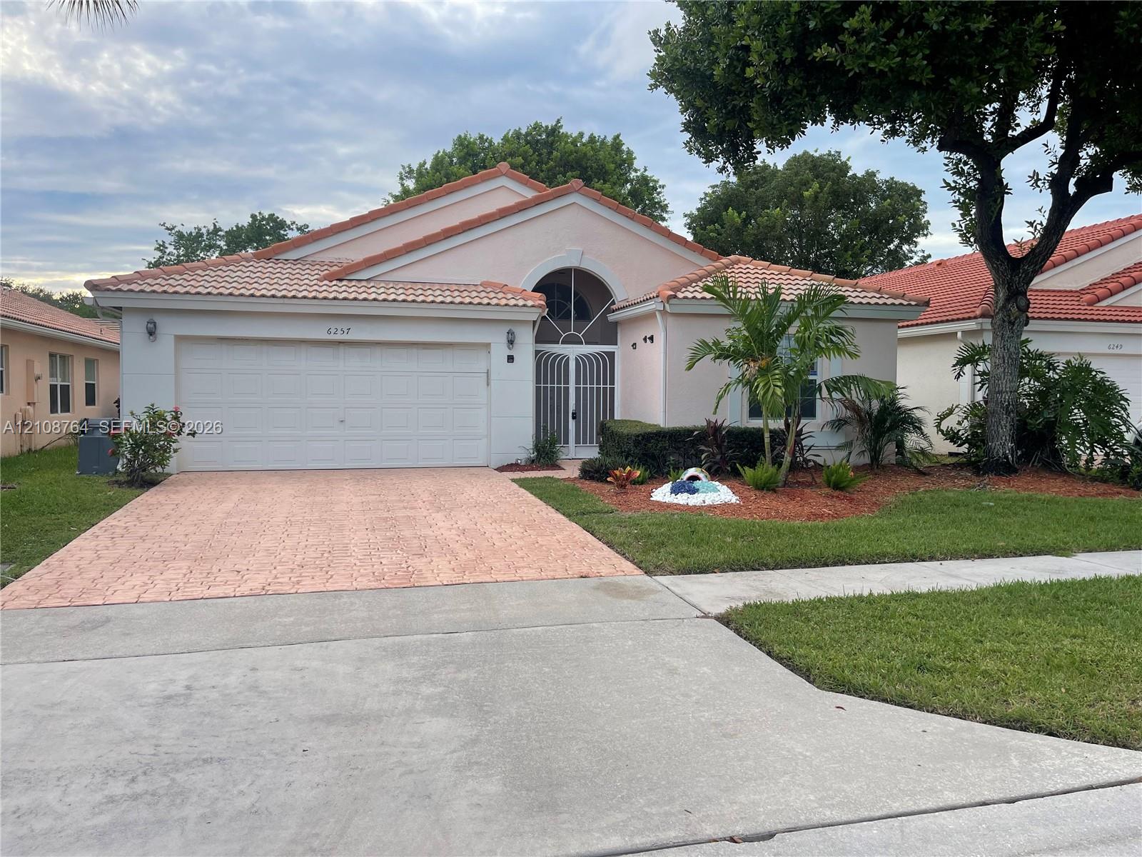 Single-story residence featuring a terracotta-tiled roof, decorative arched entryway with a security gate, two-car garage, and textured paver driveway Single-story residence featuring a terracotta-tiled roof, decorative arched entryway with a security gate, two-car garage, and textured paver driveway