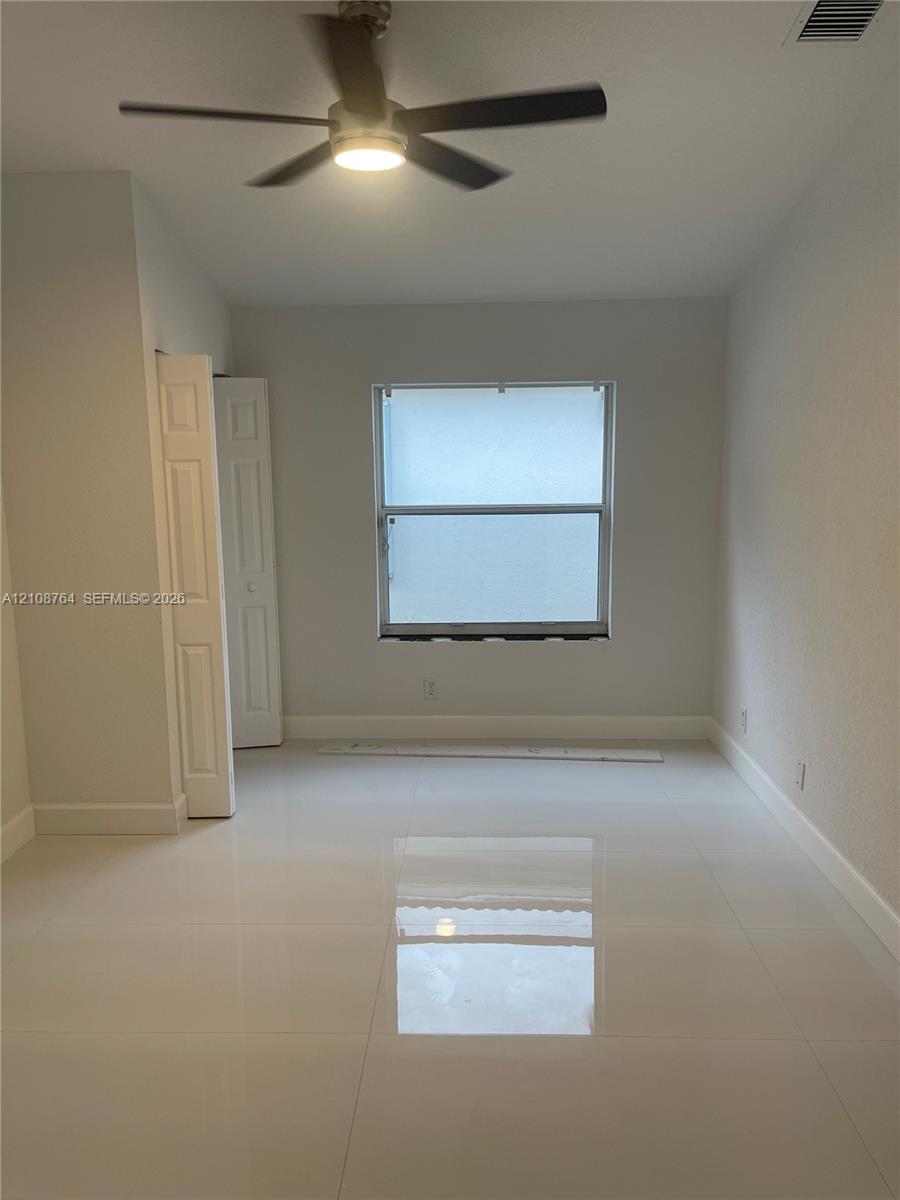 Room featuring polished tile flooring, a multi-blade ceiling fan, and a single-hung window with a closet featuring paneled doors Room featuring polished tile flooring, a multi-blade ceiling fan, and a single-hung window with a closet featuring paneled doors
