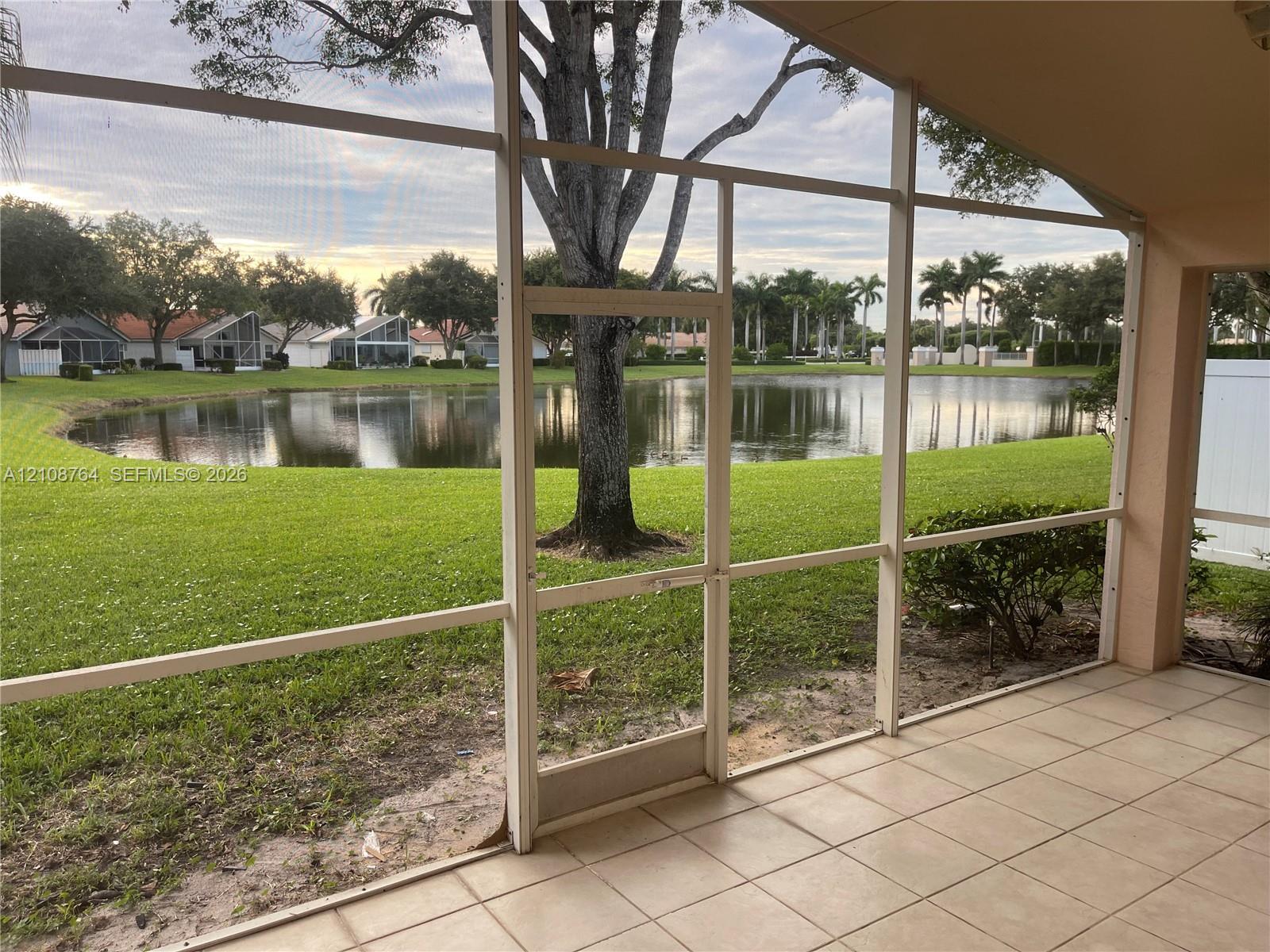 Screened lanai featuring tile flooring, aluminum framing, and direct water frontage with a lawn Screened lanai featuring tile flooring, aluminum framing, and direct water frontage with a lawn