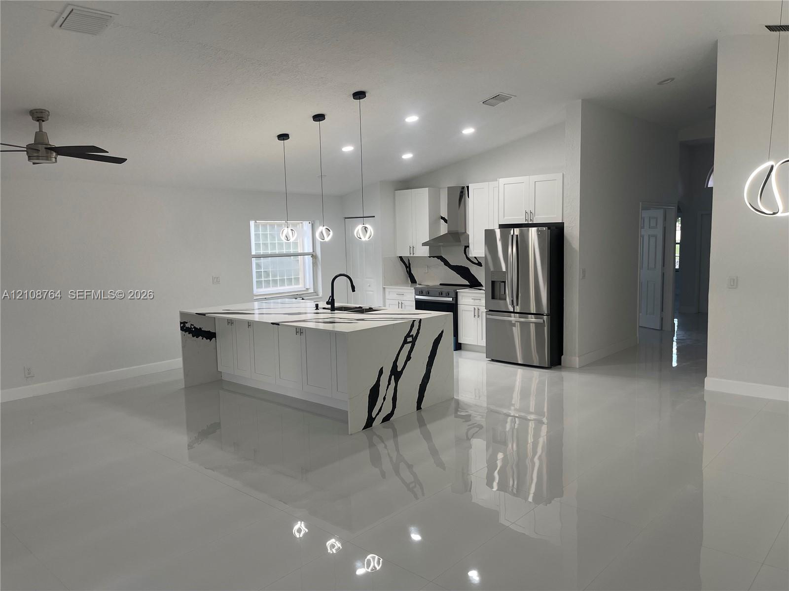 Kitchen featuring a waterfall-edge island with stone-patterned surfaces, stainless steel appliances, shaker-style cabinetry, recessed lighting, and polished tile flooring Kitchen featuring a waterfall-edge island with stone-patterned surfaces, stainless steel appliances, shaker-style cabinetry, recessed lighting, and polished tile flooring