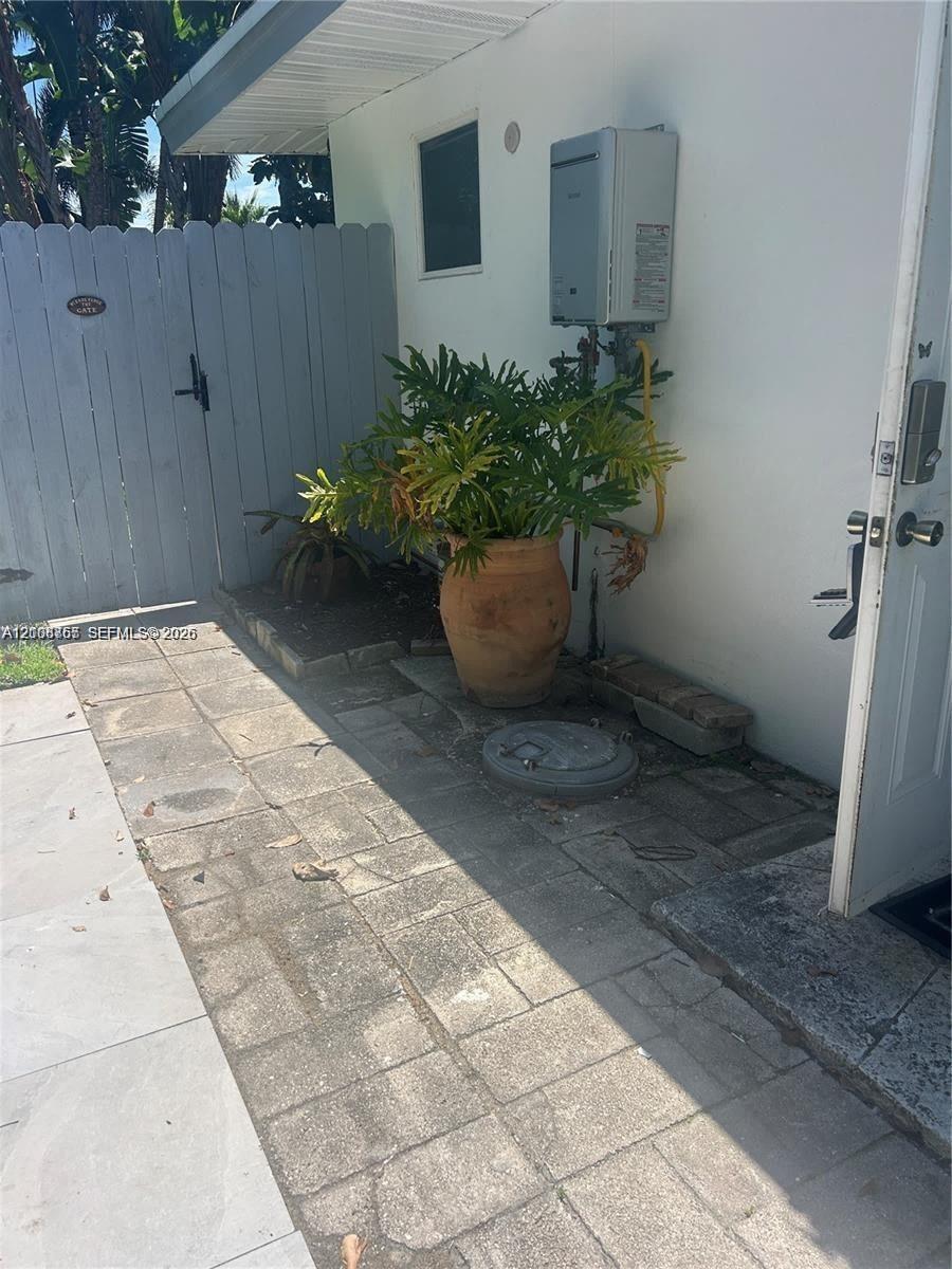 Exterior area featuring paver-stone hardscaping, wall-mounted tankless water heater, and a white privacy fence