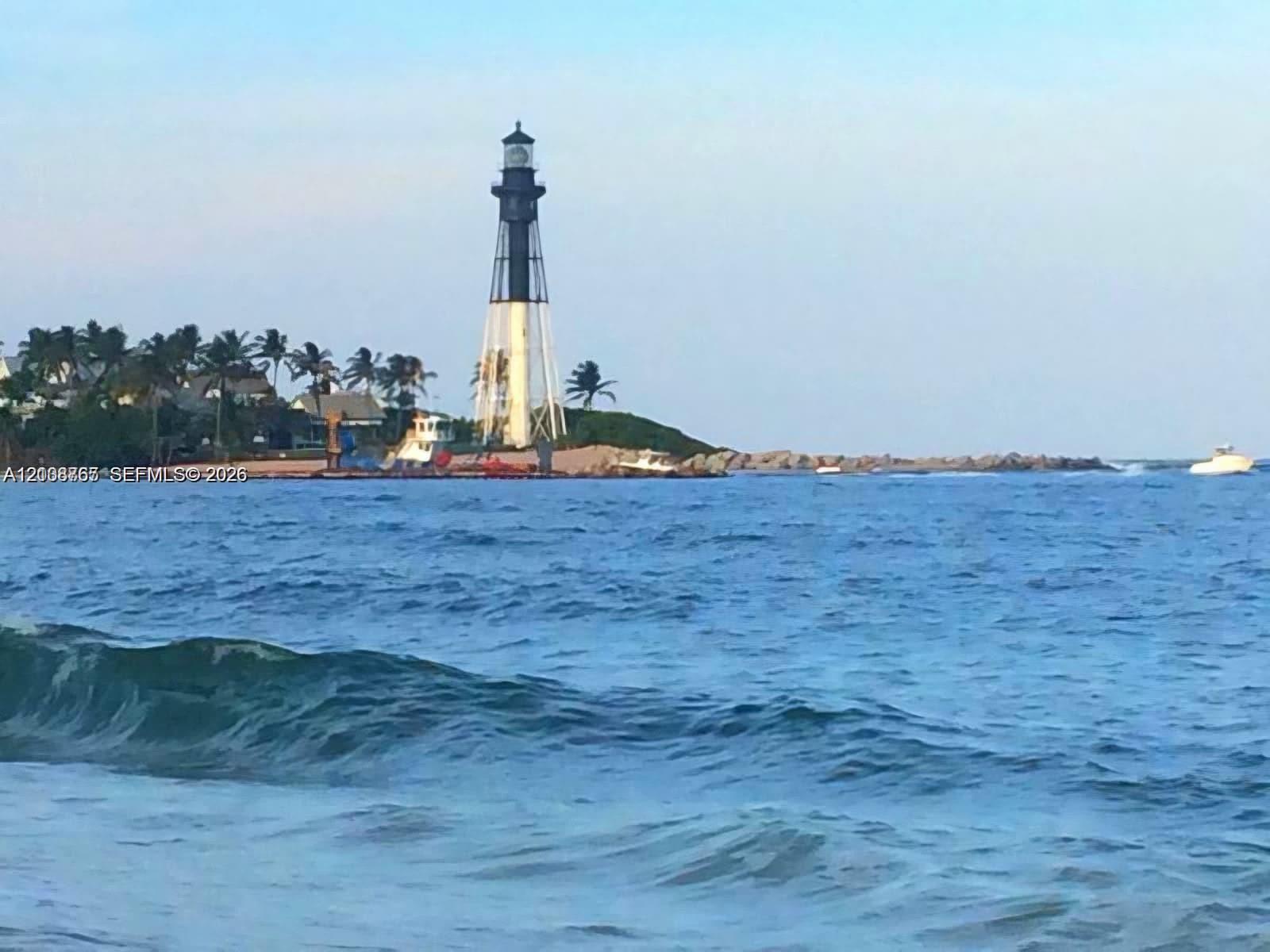 Coastal waters featuring a prominent lighthouse, palm-lined shoreline, and stone jetty