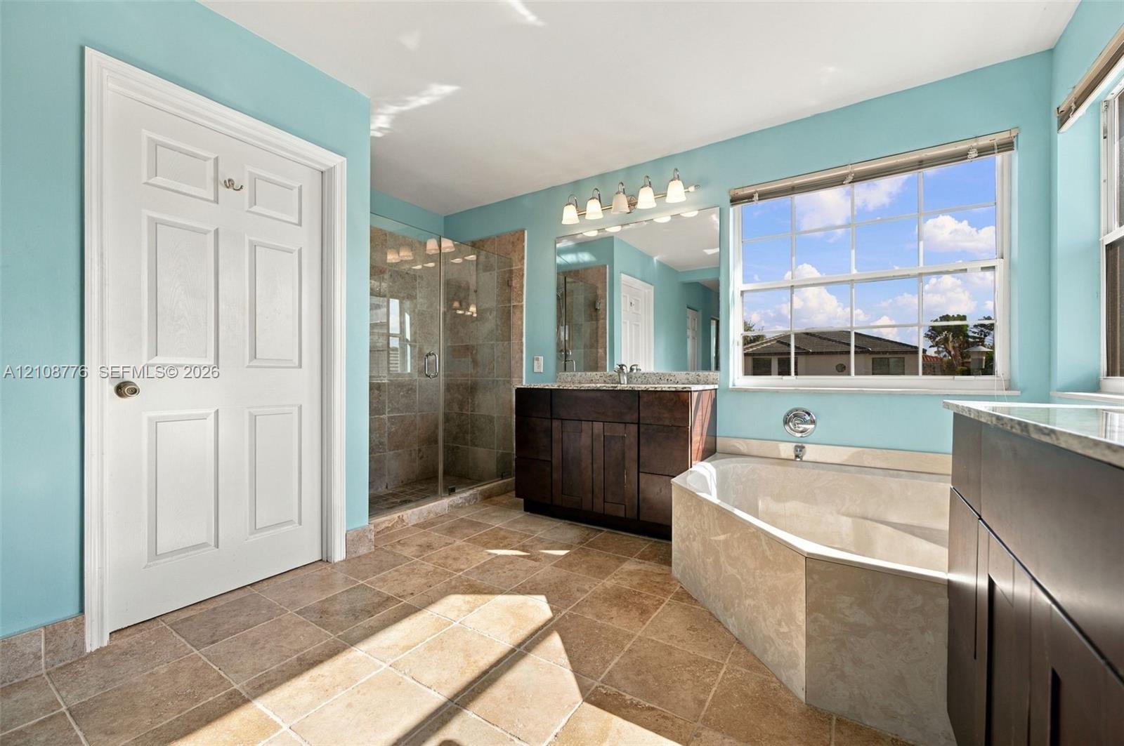 Bathroom featuring dark wood-finish cabinetry, a stone-surround soaking tub, a tiled walk-in shower with a glass enclosure, and natural stone flooring
