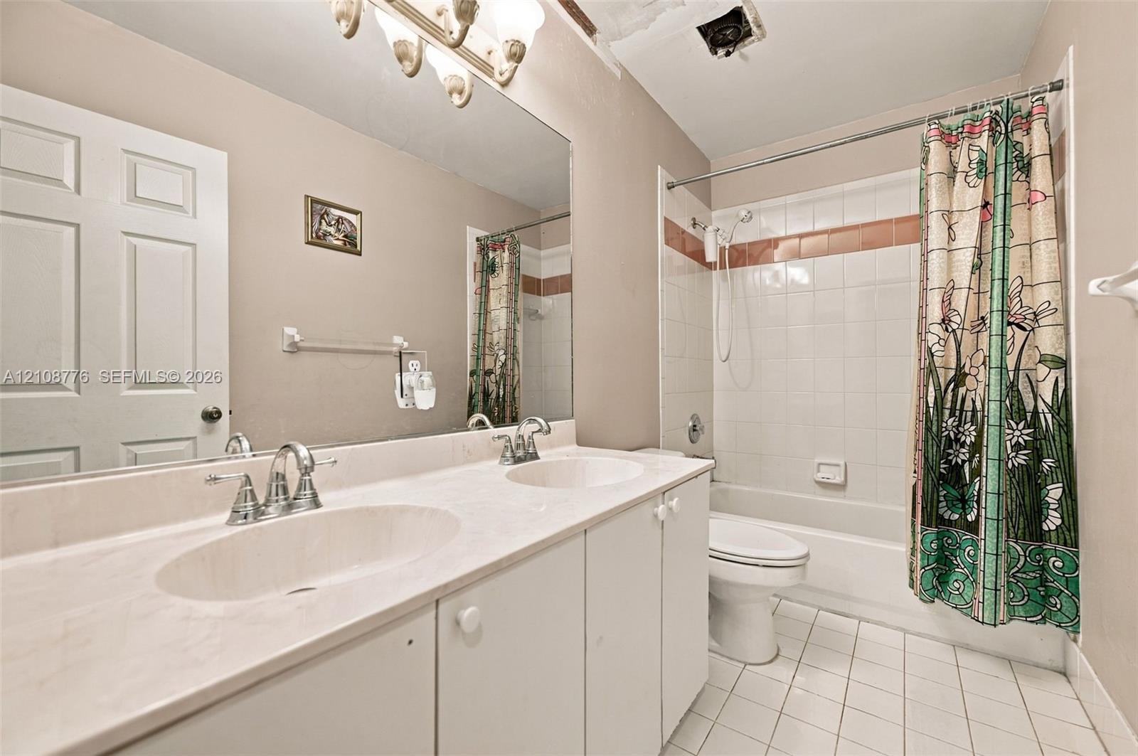 Double vanity featuring integrated oval basins, expansive wall-to-wall mirror, white cabinetry, tile-surround shower and tub combination, and ceramic tile flooring