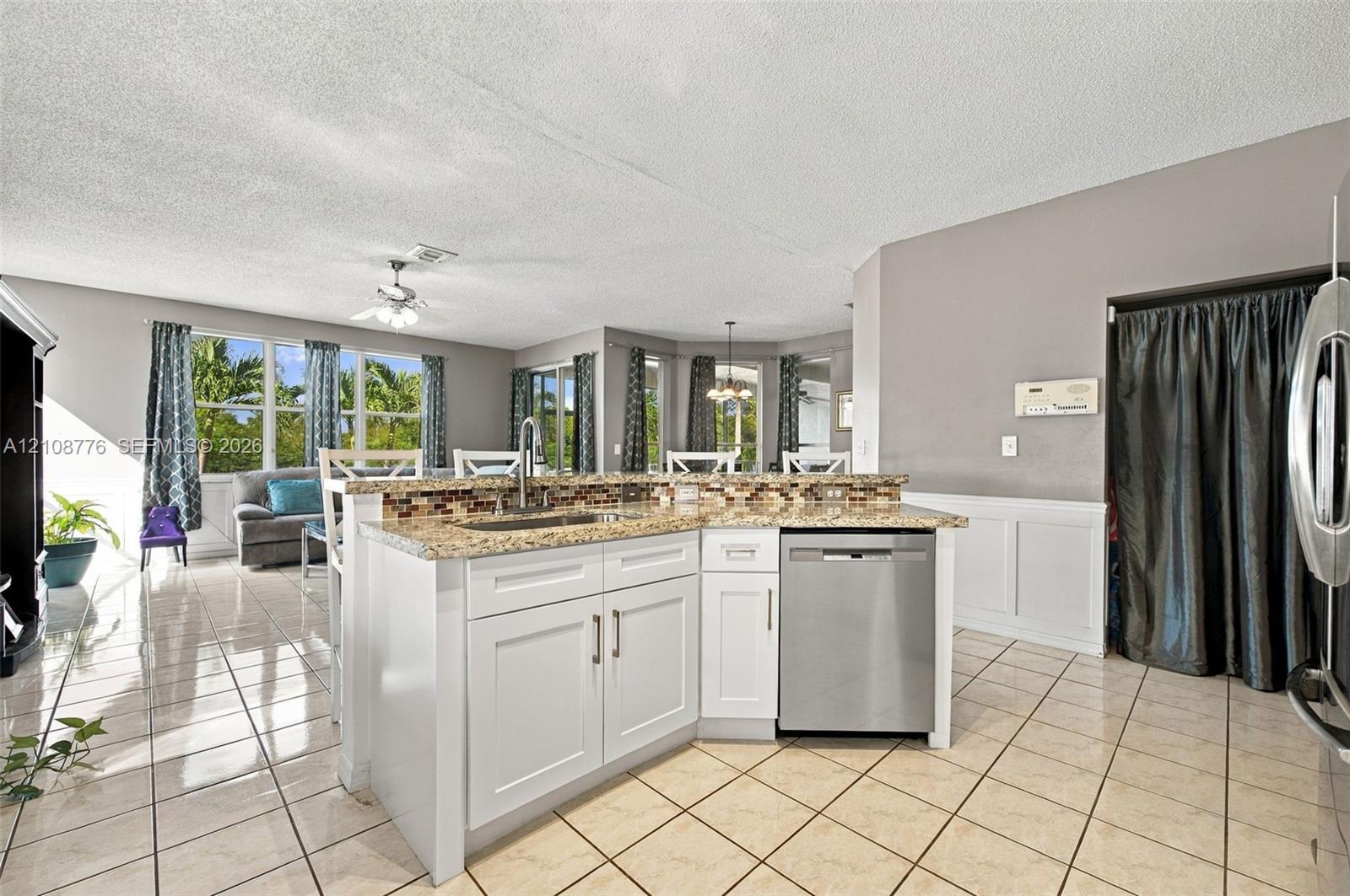 Kitchen island featuring white cabinetry, stone-finish countertops, tile backsplash, and a stainless steel dishwasher