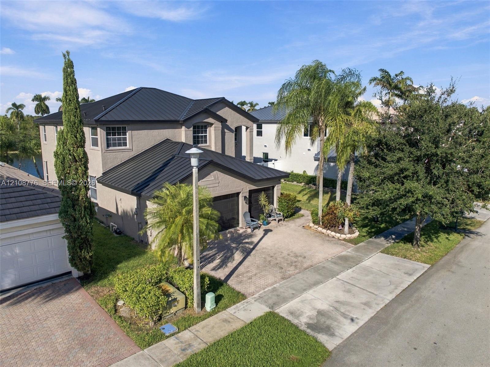 Two-story residence featuring a dark metal roof, stucco exterior, paved driveway, and attached multi-car garage