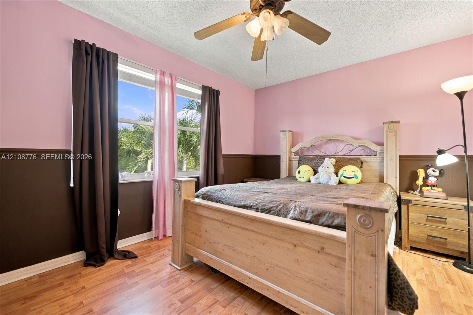 Room featuring wood-finish flooring, two-tone wall paint with a chair rail, a ceiling fan with integrated light fixture, and a large window