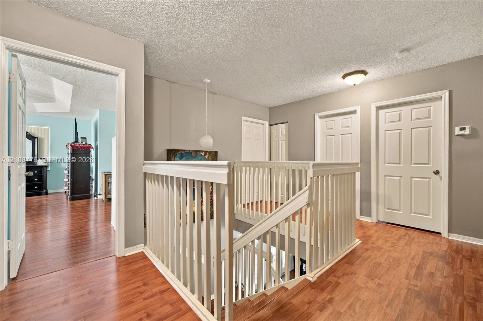 Landing featuring wood-finish flooring, white spindle railings, multi-panel interior doors, and a ceiling-mounted light fixture