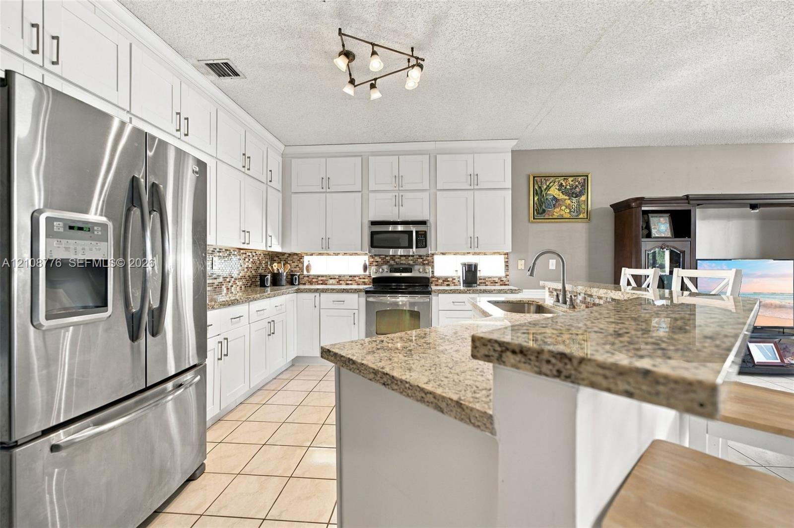 Kitchen featuring white cabinetry, stone countertops, stainless steel appliances, ceramic tile flooring, and multi-light ceiling fixture