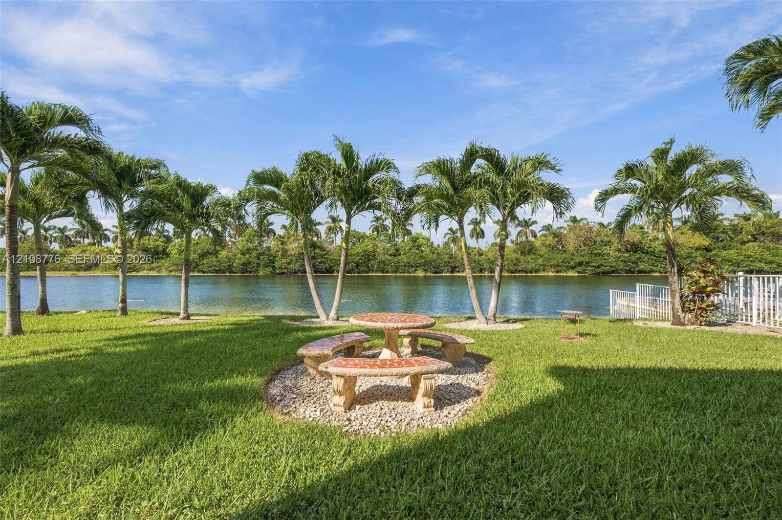 Waterfront backyard featuring a manicured lawn, palm trees, and a decorative stone-finish seating area set on a gravel bed