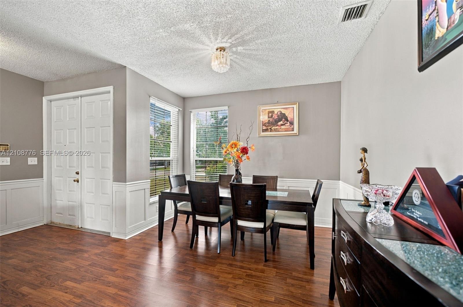 Wood-finish flooring, white wainscoting, double-panel entry door, and flush-mount crystal-style light fixture