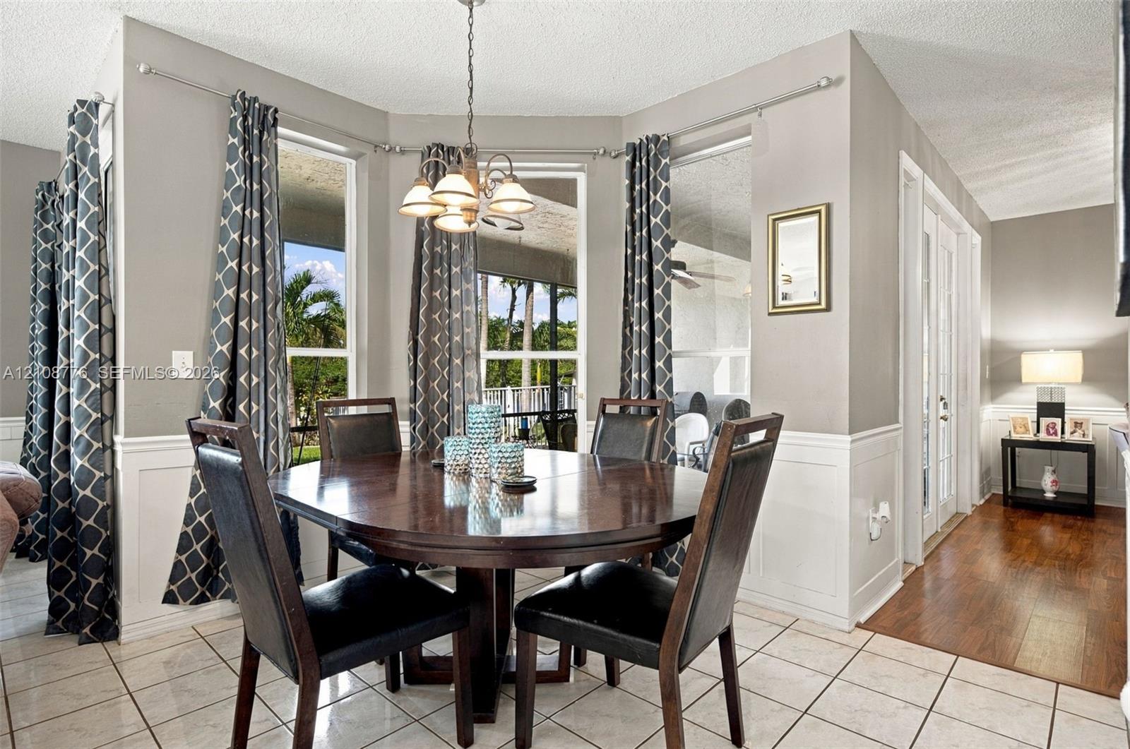 Dining area featuring a bay window, tile flooring, wainscoting, and a multi-light chandelier