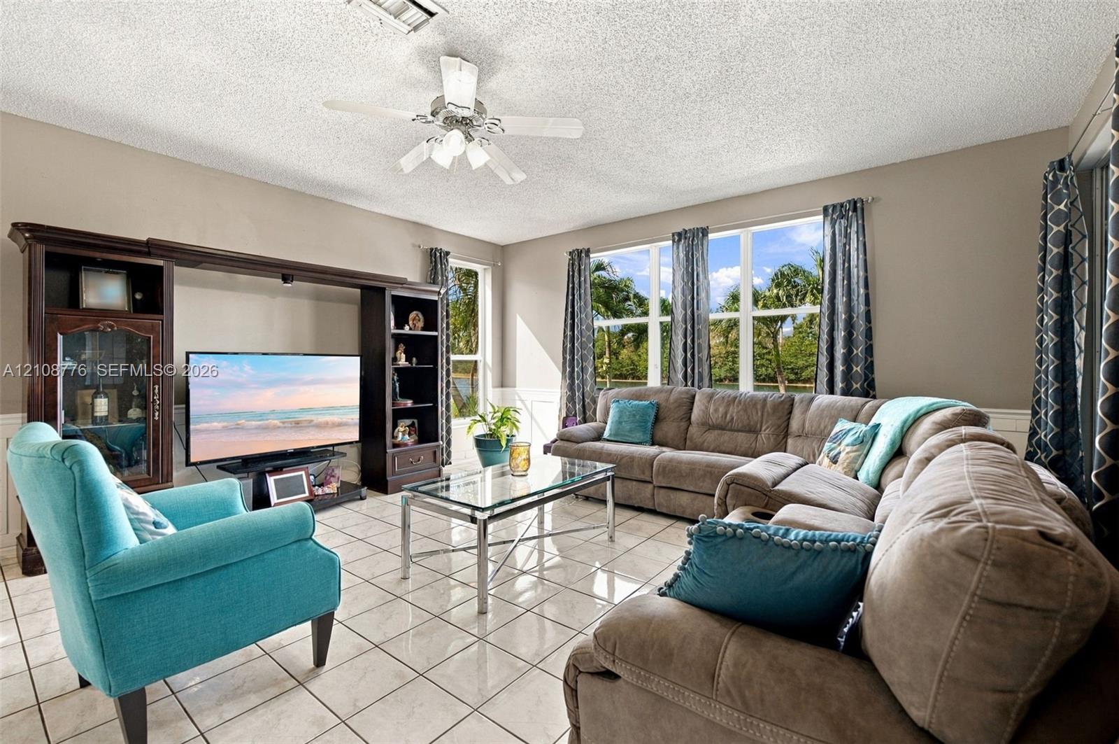Living area featuring large format tile flooring, built-in wall cabinetry, multi-pane windows, and a ceiling fan