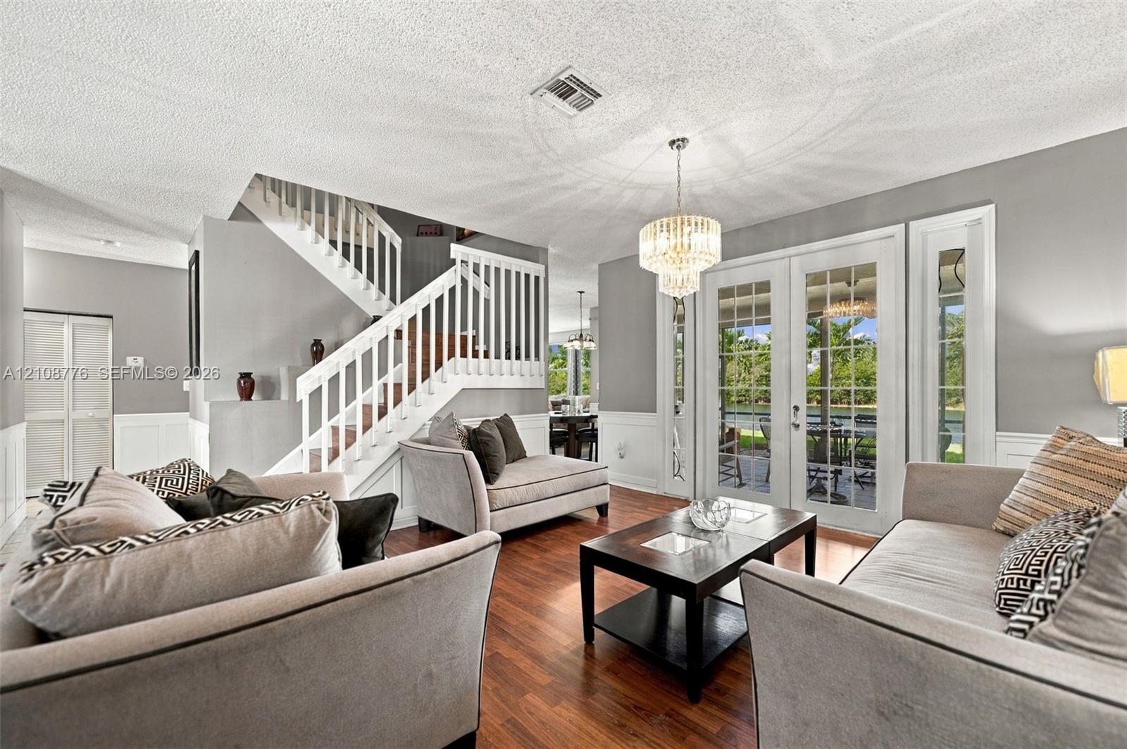 Wood-finish flooring, staircase with white railing, glass-paned French doors, tiered crystal chandelier, and wainscoting