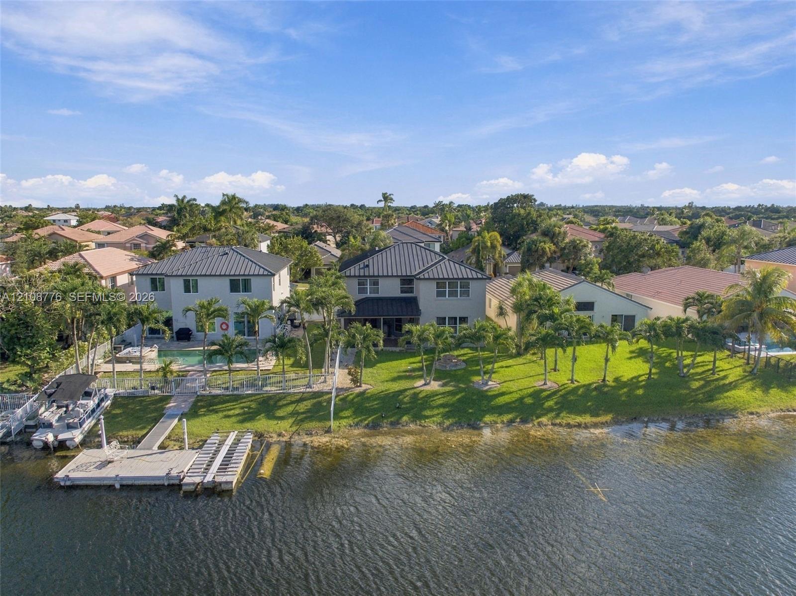 Waterfront property featuring a private boat dock, swimming pool, metal roof, and manicured lawn with mature palm trees