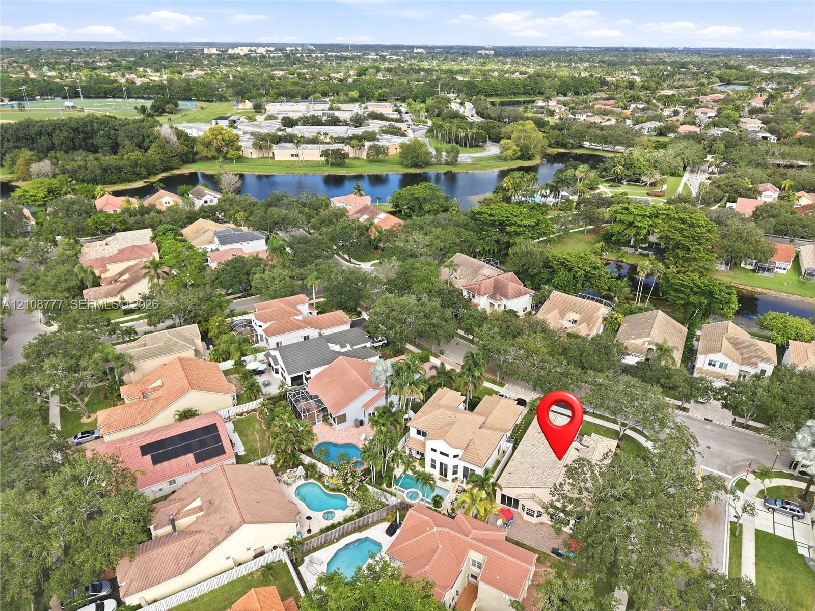 Aerial perspective showcasing a residential property with a tiled roof, paver hardscaping, and mature landscaping, situated within a master-planned community featuring multiple ponds and dense tree canopy