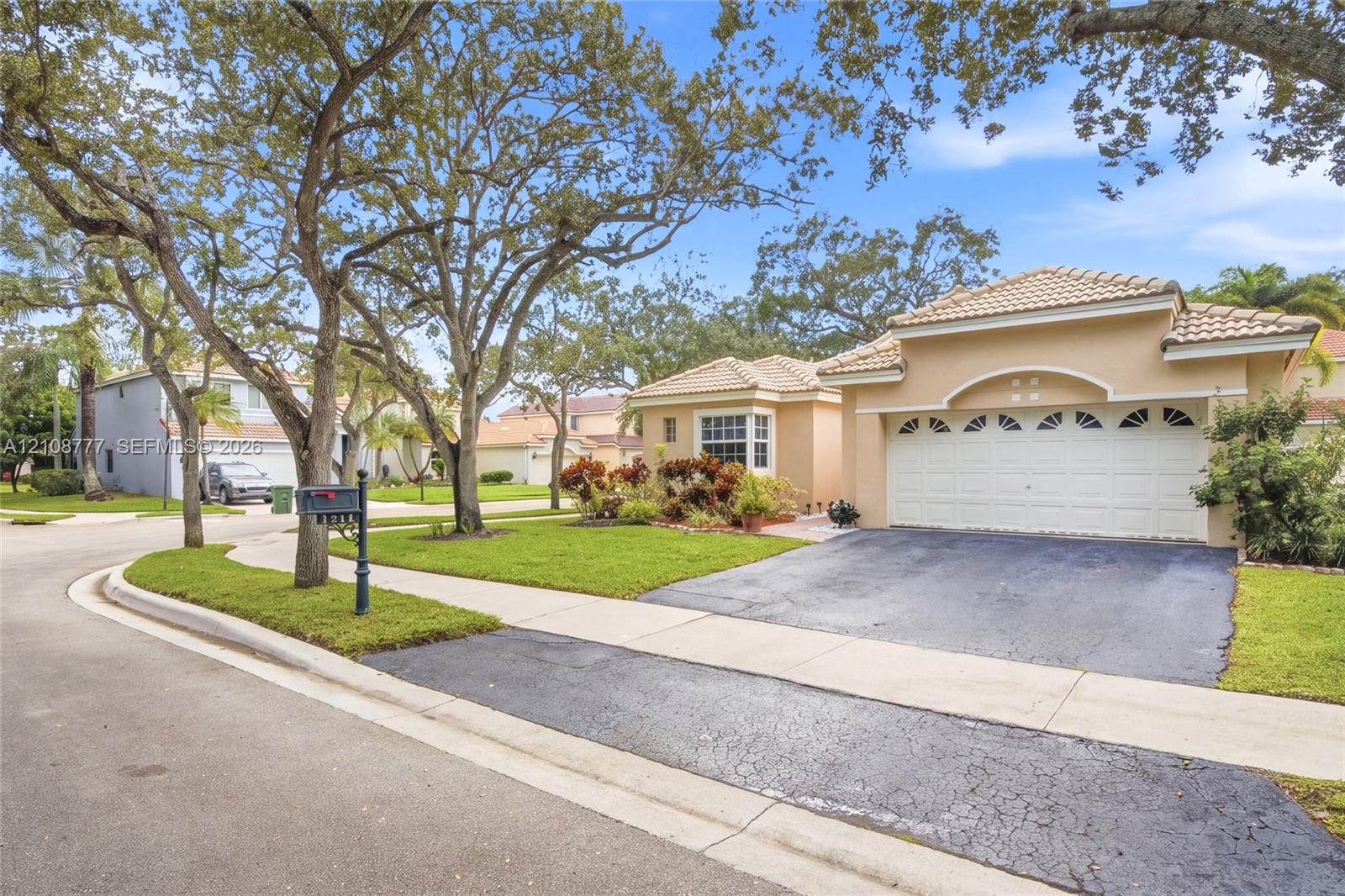 Single-story residence featuring a stucco exterior, a multi-car garage with arched decorative glass detailing, tile roofing, and mature trees