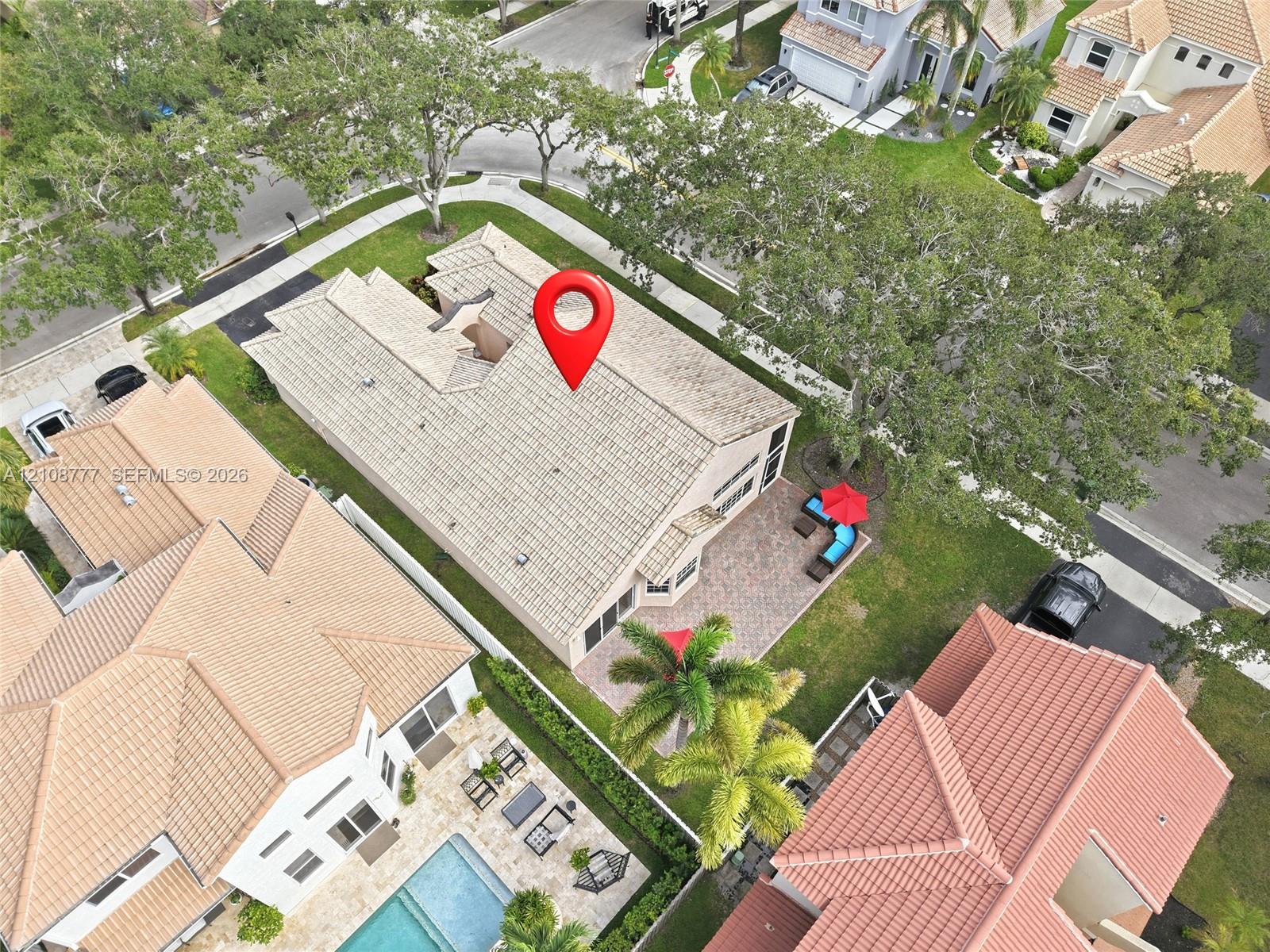 Aerial perspective of corner lot property featuring a multi-gable tiled roof, paved patio area, and established mature landscaping