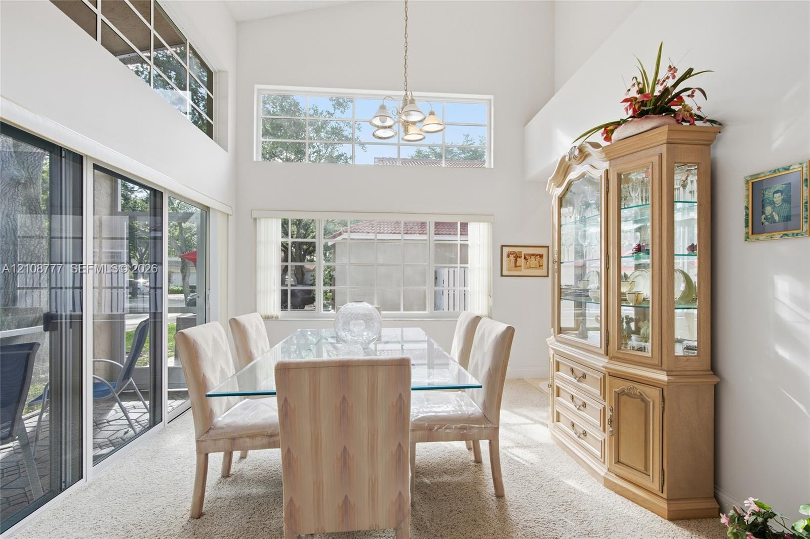 Dining area featuring vaulted ceilings, clerestory windows, multi-pane picture windows, sliding glass doors, and a decorative pendant light fixture
