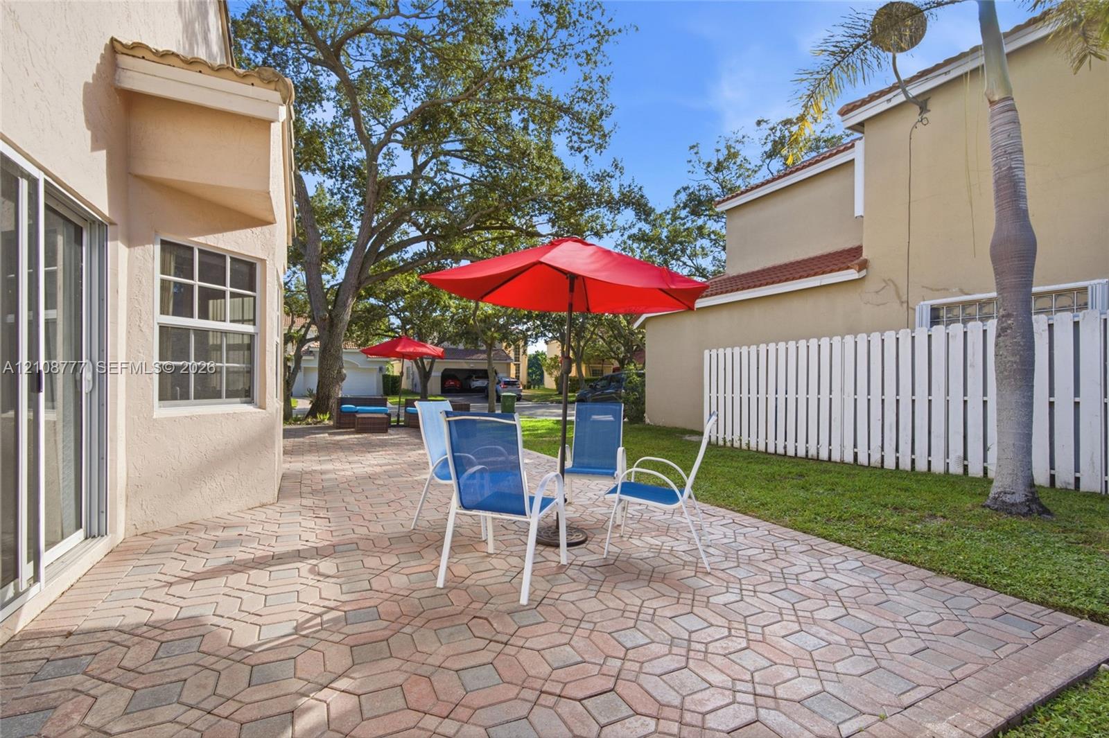 Rear exterior featuring a patterned paver patio, stucco siding, sliding glass doors, and a vertical-slat privacy fence enclosing a lawn area