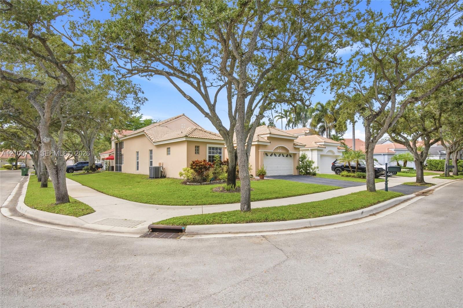 Exterior facade featuring a stucco finish, multi-gable tile roof, attached garage, and mature shade trees on a corner lot
