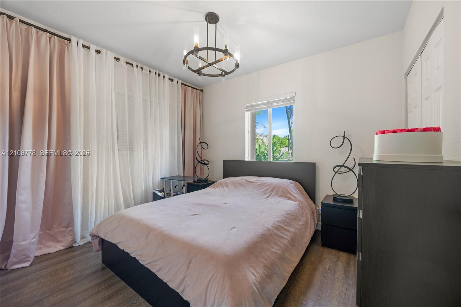 Wood-finish flooring, metal circular chandelier, window with horizontal blinds, and dual-panel closet doors