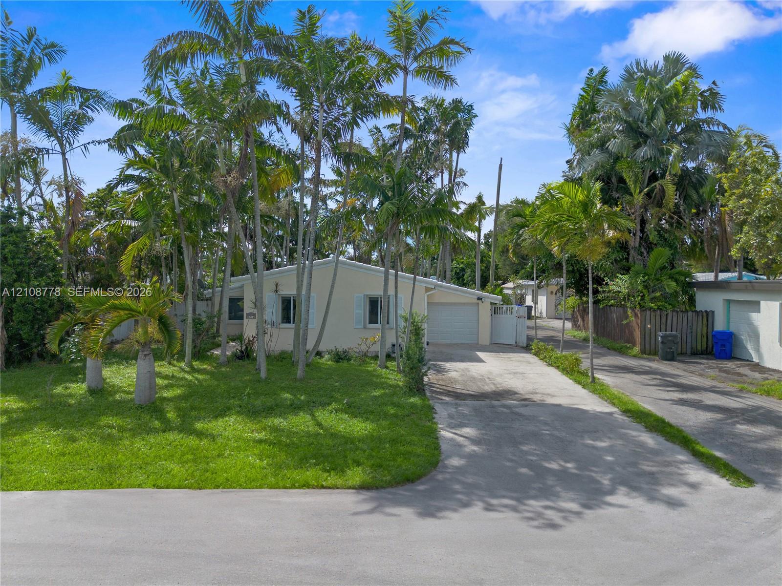 Exterior facade featuring a concrete driveway, an attached garage, mature palm trees, and established landscaping Exterior facade featuring a concrete driveway, an attached garage, mature palm trees, and established landscaping