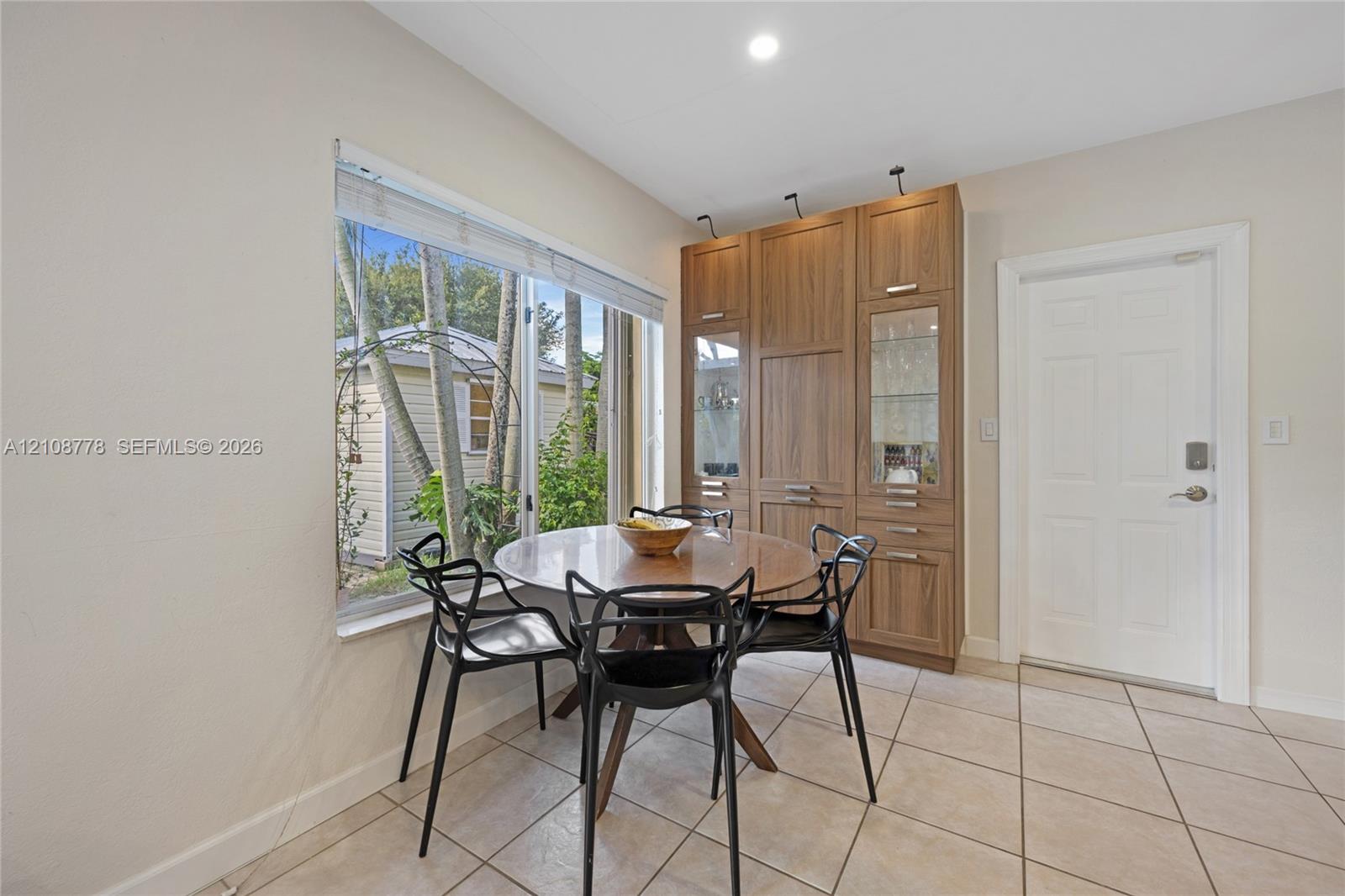 Custom built-in wood-finish cabinetry with glass display panels, large-format tile flooring, and oversized window with exterior landscape exposure