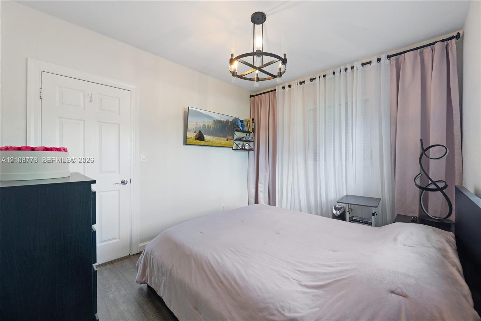 Room featuring wood-finish flooring, a matte black circular chandelier with exposed bulbs, and a six-panel interior door