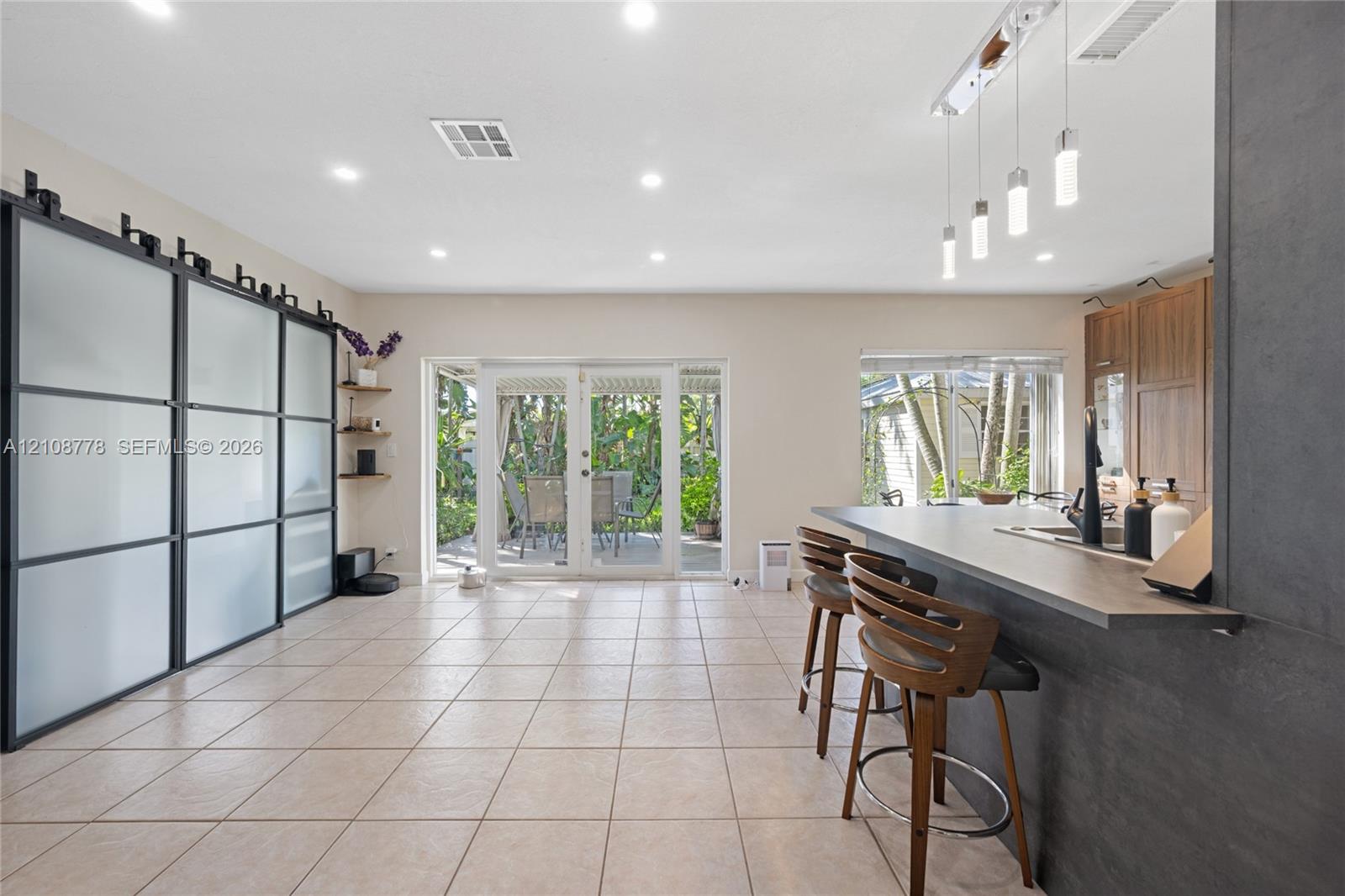 Large-format tile flooring, oversized matte black sliding partition with frosted glass panels, kitchen island with breakfast bar seating, and linear pendant lighting