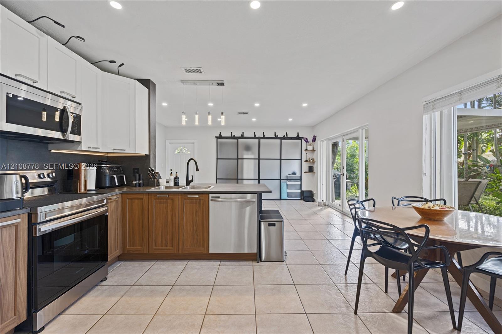 Kitchen featuring a dual-tone cabinetry design, stainless steel appliances, a peninsula with a built-in sink, recessed lighting, and large glass-panel sliding doors