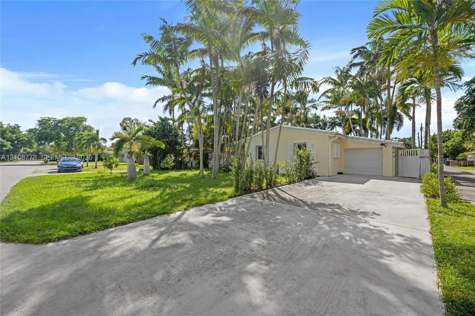 Exterior view featuring a single-story residence with an attached garage, concrete driveway, and mature palm trees