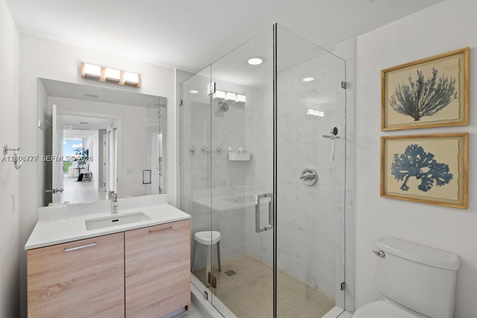 Modern vanity featuring a light wood-finish cabinet and solid-surface countertop with an integrated basin, glass-enclosed shower with wall-to-wall tiling, recessed lighting, and polished chrome fixtures