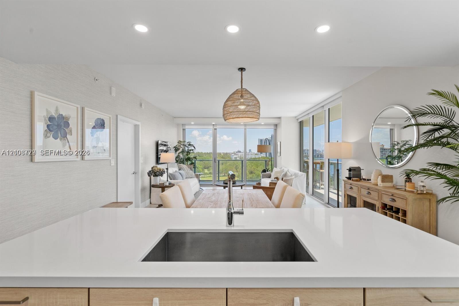 Kitchen island featuring a solid-surface countertop, under-mount stainless steel sink, and light wood-finish cabinetry, complemented by recessed ceiling lighting and floor-to-ceiling glass sliding doors Kitchen island featuring a solid-surface countertop, under-mount stainless steel sink, and light wood-finish cabinetry, complemented by recessed ceiling lighting and floor-to-ceiling glass sliding doors