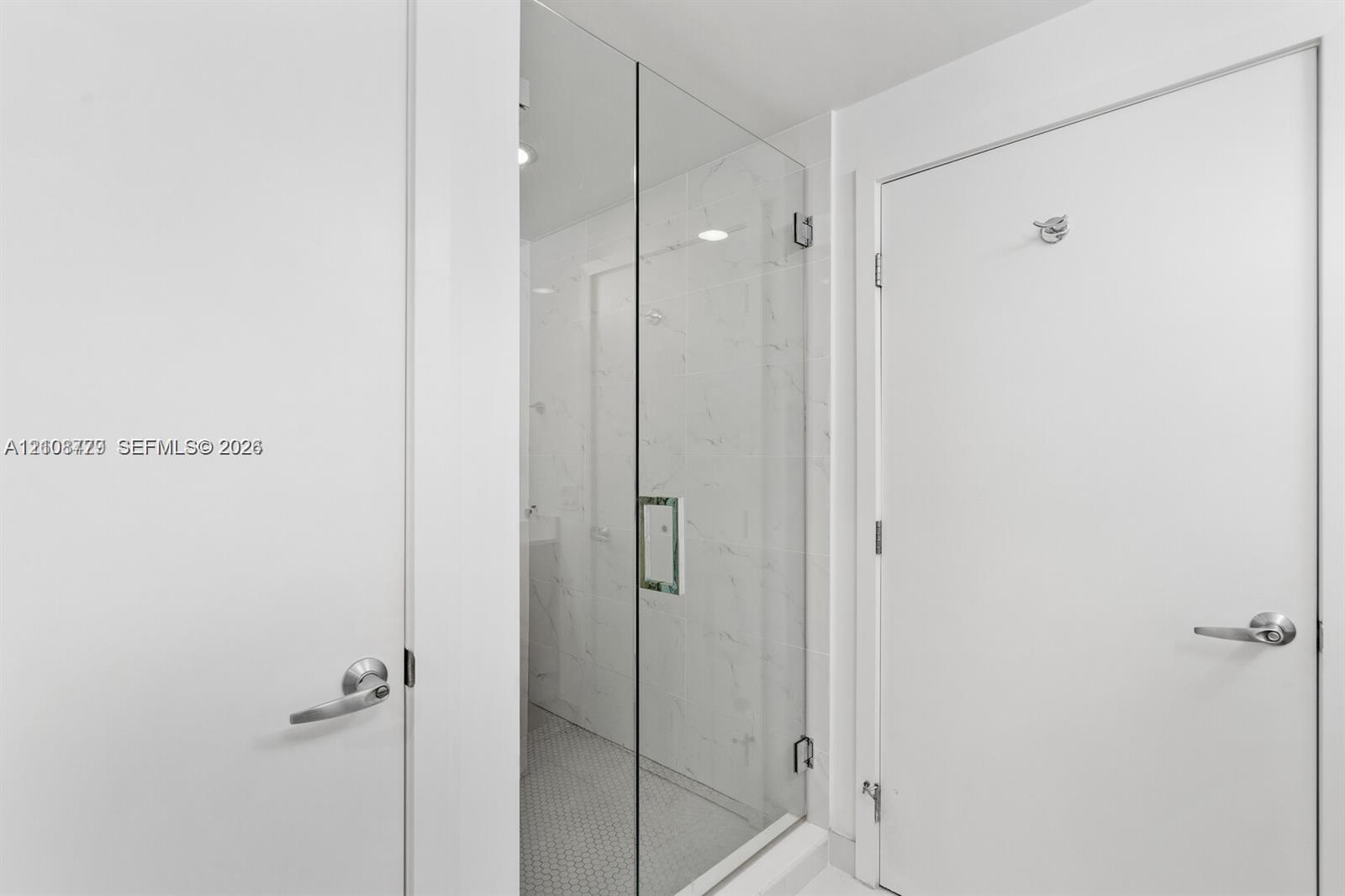 Walk-in shower featuring a frameless glass door, light-toned stone-finish tile surround, and mosaic floor tiling